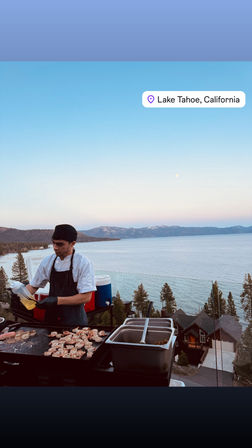 Chef grilling shrimp on an outdoor griddle with Lake Tahoe, California shoreline and mountain lake view at dusk