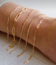 Close-up of delicate stacked gold chain bracelets on a wrist, showcasing varied minimal link styles for layered everyday jewelry.