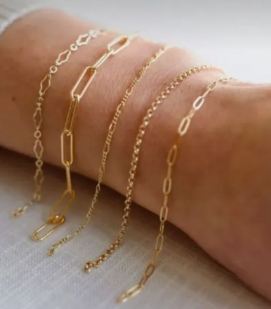 Close-up of delicate stacked gold chain bracelets on a wrist, showcasing varied minimal link styles for layered everyday jewelry.