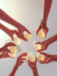 Low-angle shot of a group toast indoors — multiple hands with bracelets and rings holding up plastic cups of pale yellow drinks, festive gathering vibe.