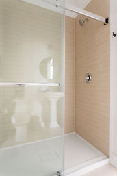 Modern walk-in bathroom shower with beige subway tiles, sliding glass door, chrome showerhead and white shower pan.