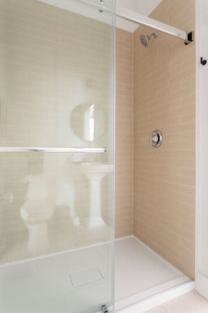Modern walk-in bathroom shower with beige subway tiles, sliding glass door, chrome showerhead and white shower pan.