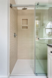 Clean, spa-like walk-in shower with beige horizontal subway tiles, two recessed niches, chrome rain showerhead and control, glass sliding door and white shower pan