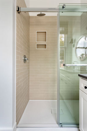 Clean, spa-like walk-in shower with beige horizontal subway tiles, two recessed niches, chrome rain showerhead and control, glass sliding door and white shower pan