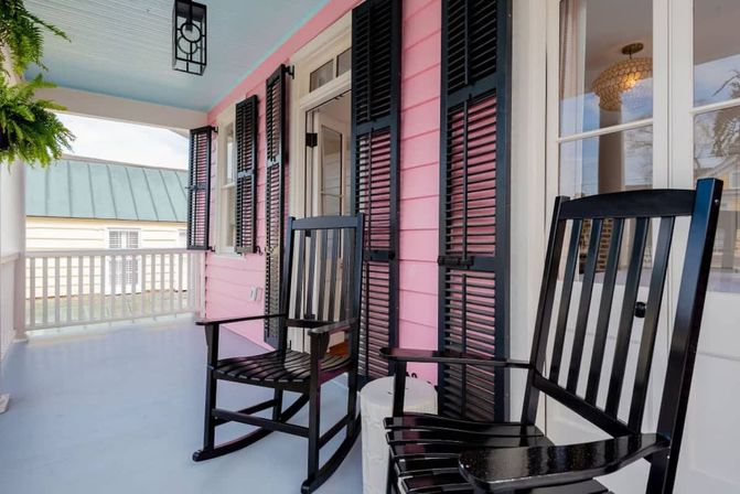 Cheerful pink front porch with pale-blue ceiling, black shutters and two black rocking chairs beside a hanging fern.