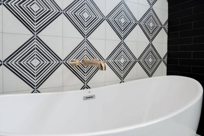 Contemporary bathroom with white freestanding tub, wall-mounted brass faucet, and bold black-and-white geometric diamond-pattern tiles.
