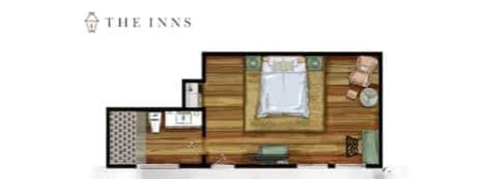 Top-down hotel room floor plan of a cozy studio layout: central bed on rug with nightstands, seating nook with armchair and side table, TV bench at foot of bed, and a small bathroom with sink and toilet on wood floors.
