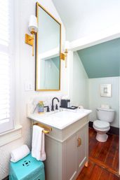 Bright small bathroom with marble-topped vanity, gold-framed mirror and sconces, matte-black faucet, mint-green beadboard walls, white toilet, and warm wood floor — chic coastal-style powder room.