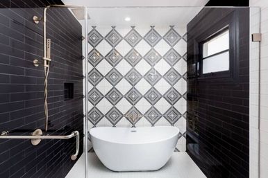 Contemporary bathroom with a white freestanding oval tub centered against a black-and-white geometric diamond tile accent wall, flanked by glossy black subway-tiled shower walls, glass enclosure, and brushed metal shower fixtures.