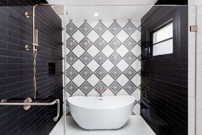 Contemporary bathroom with a white freestanding oval tub centered against a black-and-white geometric diamond tile accent wall, flanked by glossy black subway-tiled shower walls, glass enclosure, and brushed metal shower fixtures.