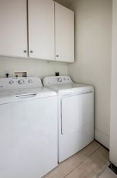 Clean home laundry nook with matching white top-load washer and front-load dryer beneath white wall cabinets on a tiled floor.