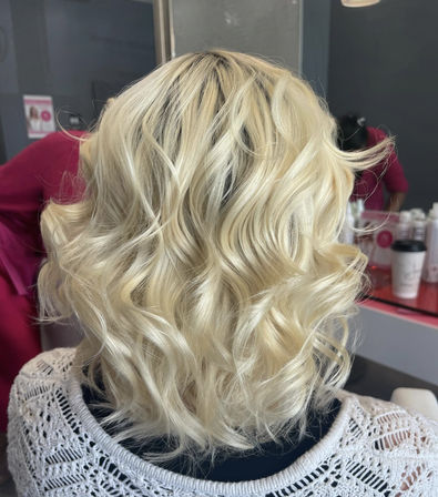 Back view of shoulder-length platinum blonde wavy bob with soft beachy curls in a salon mirror setting