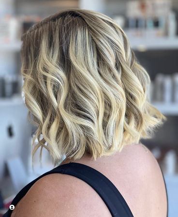 Sun-kissed blonde wavy lob — shoulder-length textured bob with soft beachy waves, styled in a salon setting