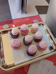 Assorted mini cupcakes with pink frosting and white nonpareil sprinkles on a silver serving tray over a pink countertop, bite-size vanilla and chocolate desserts display