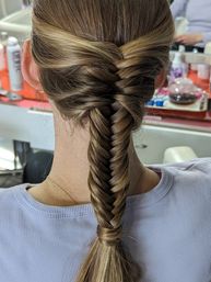 Sleek fishtail braid on highlighted brown hair, back view in a hair salon setting with a lavender top visible