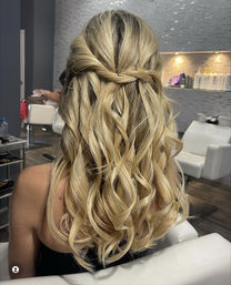 Blonde half-up twisted hairstyle with loose beachy curls, back view in a modern salon setting