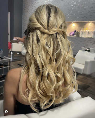 Blonde half-up twisted hairstyle with loose beachy curls, back view in a modern salon setting