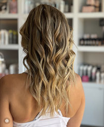Sun-kissed blonde balayage with loose beachy waves on shoulder-length hair, photographed from the back in a bright salon setting.