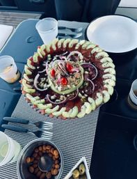 Vibrant tuna carpaccio and avocado salad arranged in concentric rings with cherry tomatoes, red onion and sesame on a platter, served on a boat table with olives and nuts