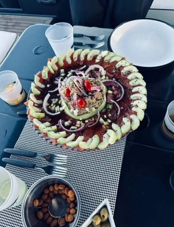 Vibrant tuna carpaccio and avocado salad arranged in concentric rings with cherry tomatoes, red onion and sesame on a platter, served on a boat table with olives and nuts