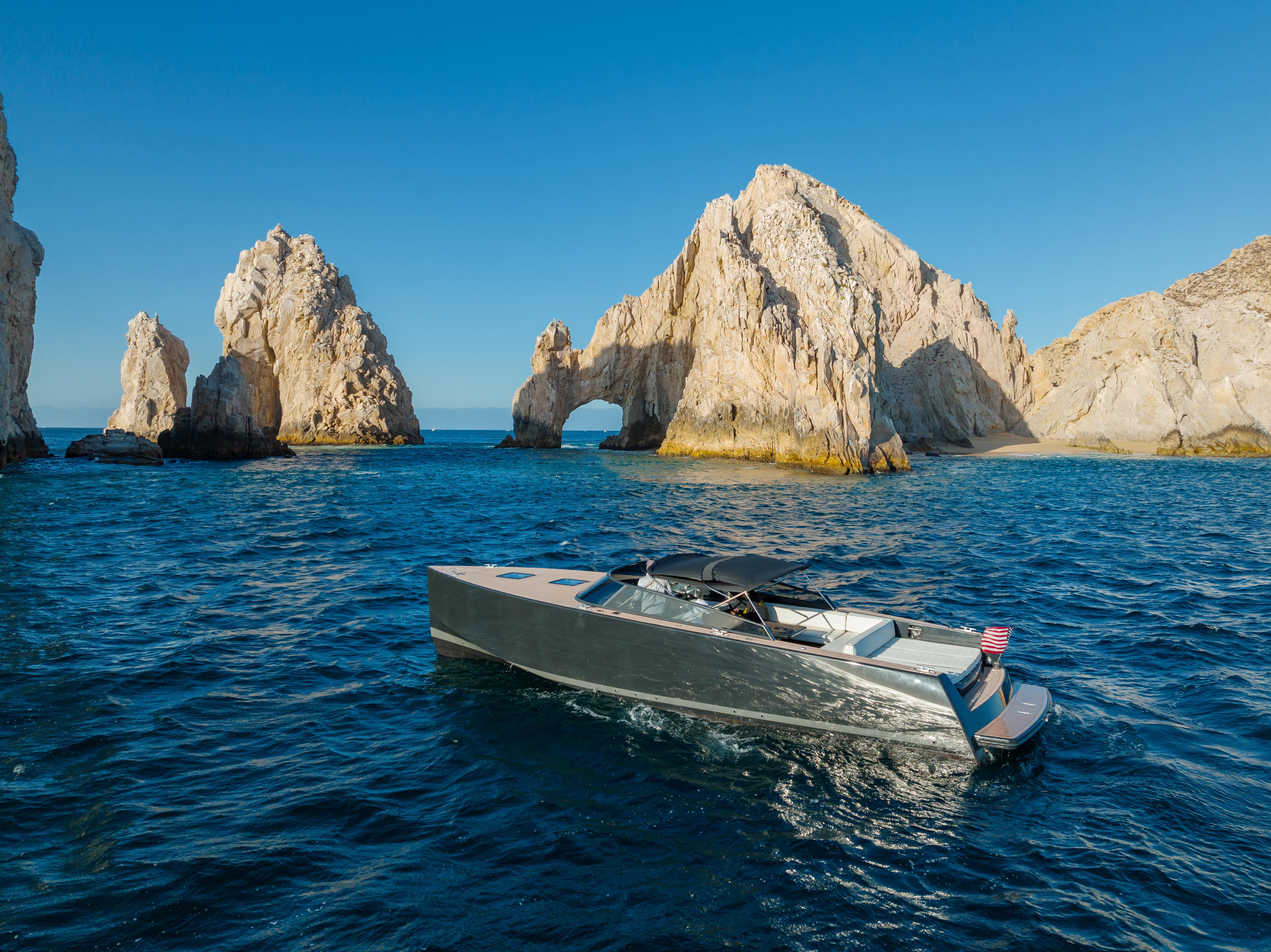 Sleek motorboat cruising blue Pacific waters beside El Arco rock arch at Land’s End, Cabo San Lucas, Mexico, under a clear sky.