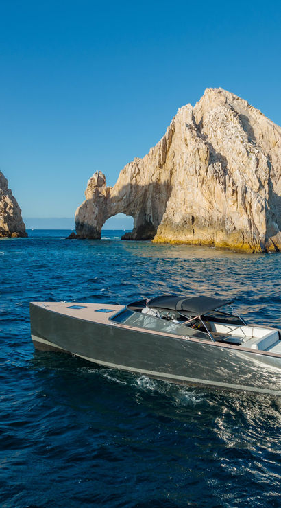 Sleek motorboat cruising blue Pacific waters beside El Arco rock arch at Land’s End, Cabo San Lucas, Mexico, under a clear sky.