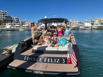 Group of women relaxing and waving on the deck of a motor yacht in a sunny marina harbor, surrounded by yachts, docks and waterfront buildings under a clear blue sky — upbeat vacation vibe