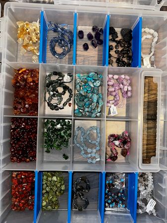 Clear plastic compartment organizer filled with colorful gemstone and glass beads sorted by color — turquoise, purple, amber, green and red — ready for jewelry making and beading projects.