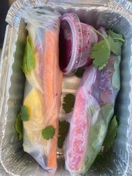 Bright Vietnamese-style rice paper spring rolls with carrots, leafy greens and cilantro, served with vivid beet-purple dipping sauce in a foil takeout tray
