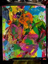Close-up of a vibrant abstract impasto canvas painting with thick textured strokes of orange, pink, green, blue and metallic gold, propped on an outdoor easel.