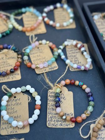 Colorful handmade gemstone and lava bead bracelets on kraft paper tags arranged on a black display tray at an artisan market stall