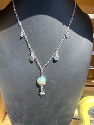 Silver chain necklace with round labradorite charms and a dangling star pendant displayed on a black jewelry bust in sunlight