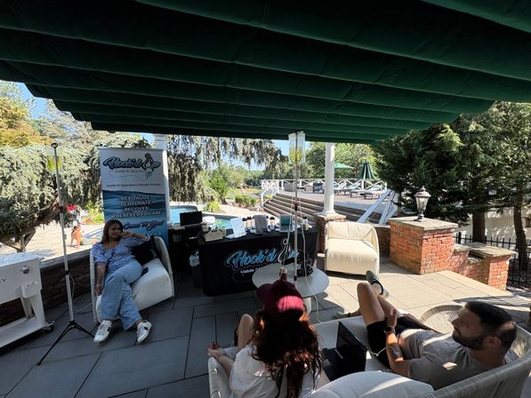 Poolside shaded patio wellness pop-up with IV drip stations and relaxed guests lounging on outdoor sofas