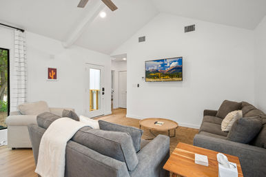 Bright vaulted-ceiling living room with gray sofas, striped armchair, wall-mounted TV and round wooden coffee table on hardwood floors