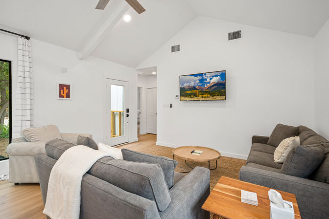 Bright vaulted-ceiling living room with gray sofas, striped armchair, wall-mounted TV and round wooden coffee table on hardwood floors