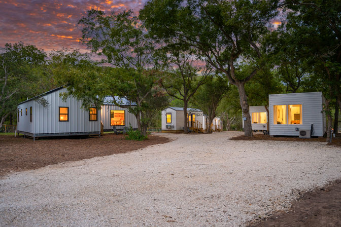 Cozy modern tiny cabin rentals with glowing windows along a gravel driveway in a wooded sunset retreat