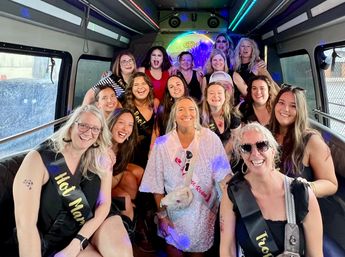 Group of smiling women on a colorful party bus celebrating a bachelorette, wearing sashes and festive outfits under LED lights.