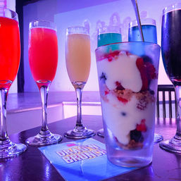 Row of colorful champagne cocktails and a berry yogurt parfait on a table at a purple-lit drag brunch