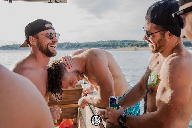 Shirtless friends laughing on a sunny lake boat ride, two in backward caps and sunglasses, one leaning over the rail