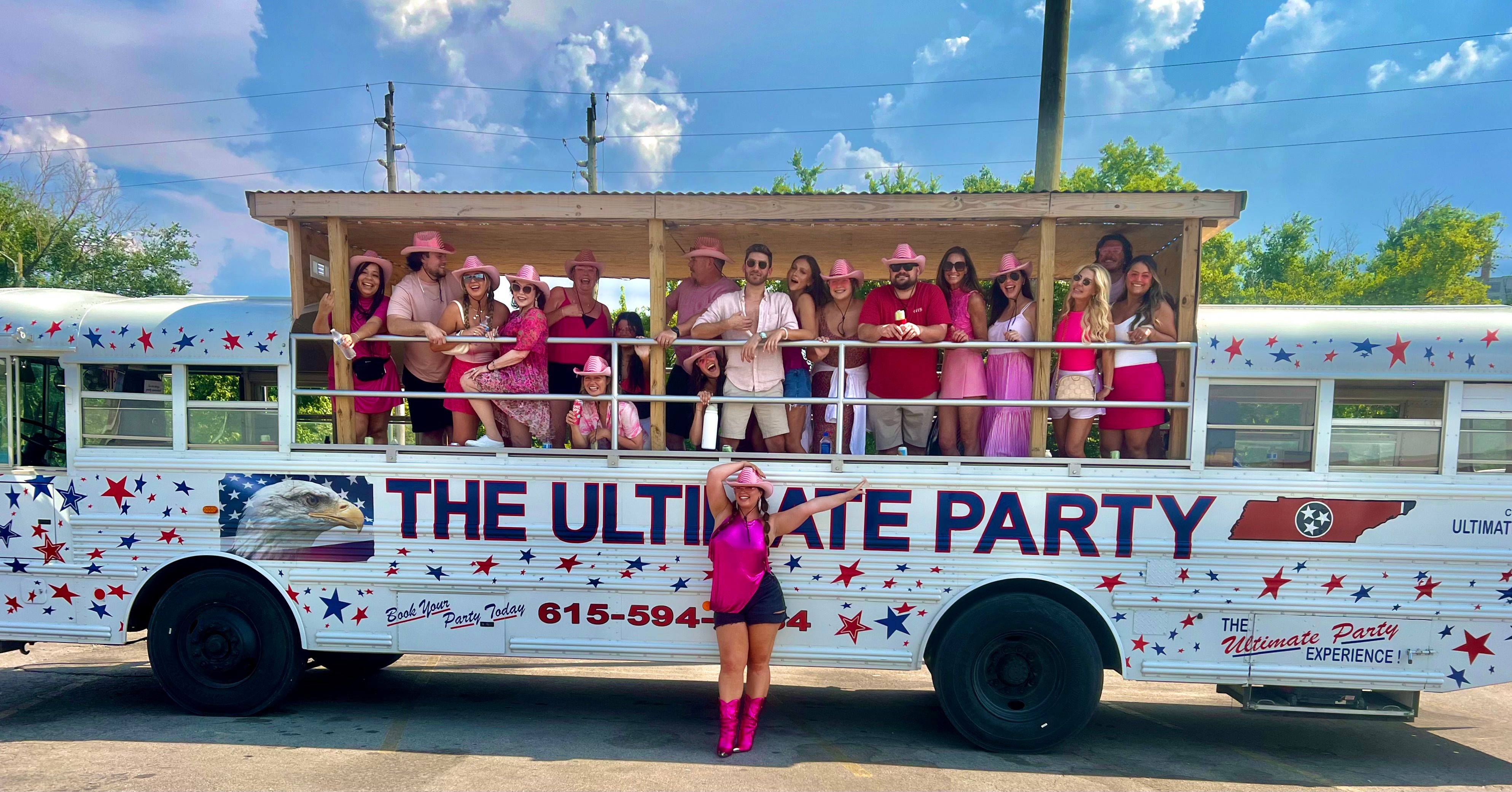 Group of friends in pink outfits and cowboy hats partying on an open-sided, star-spangled Tennessee-themed party bus under a bright summer sky; woman in shiny pink boots poses in front.