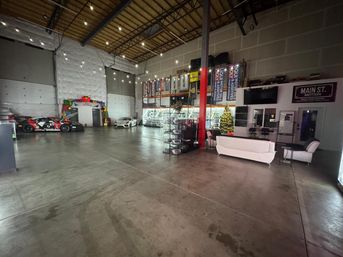 Spacious industrial warehouse car showroom with race cars, display shelving, lounge seating, string lights and a decorated Christmas tree.