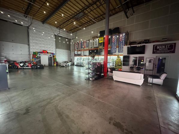 Spacious industrial warehouse car showroom with race cars, display shelving, lounge seating, string lights and a decorated Christmas tree.