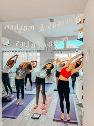 Group of women doing side-stretch yoga on mats in a bright, modern living room with decorative banners overhead — energetic home yoga session.