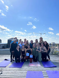 Group of women in athletic wear posing on rooftop yoga mats during an outdoor rooftop yoga class with an urban skyline and construction crane under a bright blue sky.