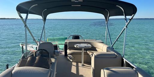 Pontoon boat with navy canopy, cushioned beige seating and a small table, floating over crystal-clear turquoise water under a sunny blue sky.