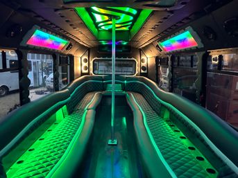 Vibrant party bus interior with curved quilted leather bench seating, center dance pole, neon green and rainbow LED accent lighting and windows.