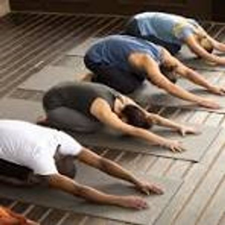 Indoor group yoga class practicing child's pose on mats lined up on a wooden floor