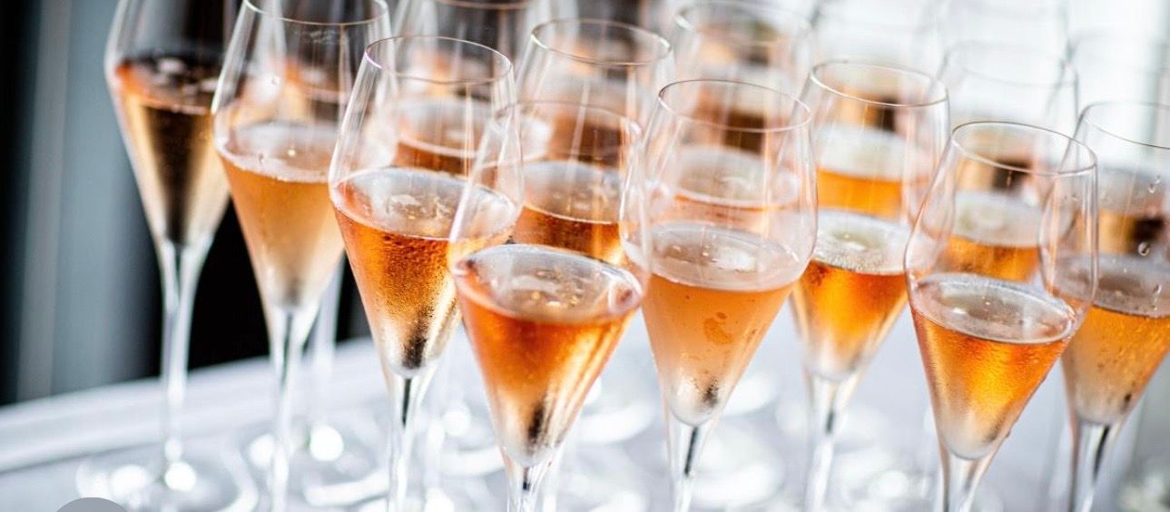 Cluster of chilled rosé sparkling wine flutes with bubbles on a white table, ready for a celebration or reception
