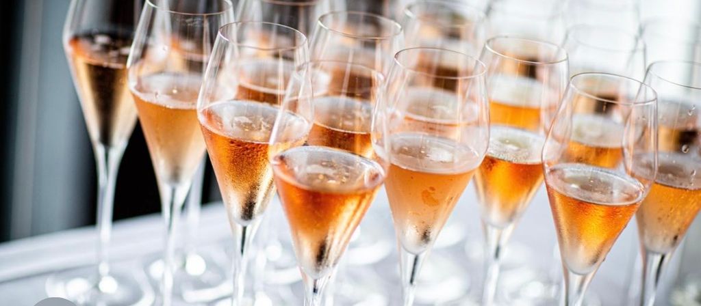 Cluster of chilled rosé sparkling wine flutes with bubbles on a white table, ready for a celebration or reception