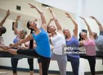 Group of women in a bright indoor fitness studio doing a ballet-inspired barre class, practicing balance and stretch exercises
